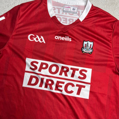 A close-up of a red and white striped GAA jersey with 'oneills' and the 'GAA' logo on the chest, featuring a large 'SPORTS DIRECT' sponsor logo across the front.